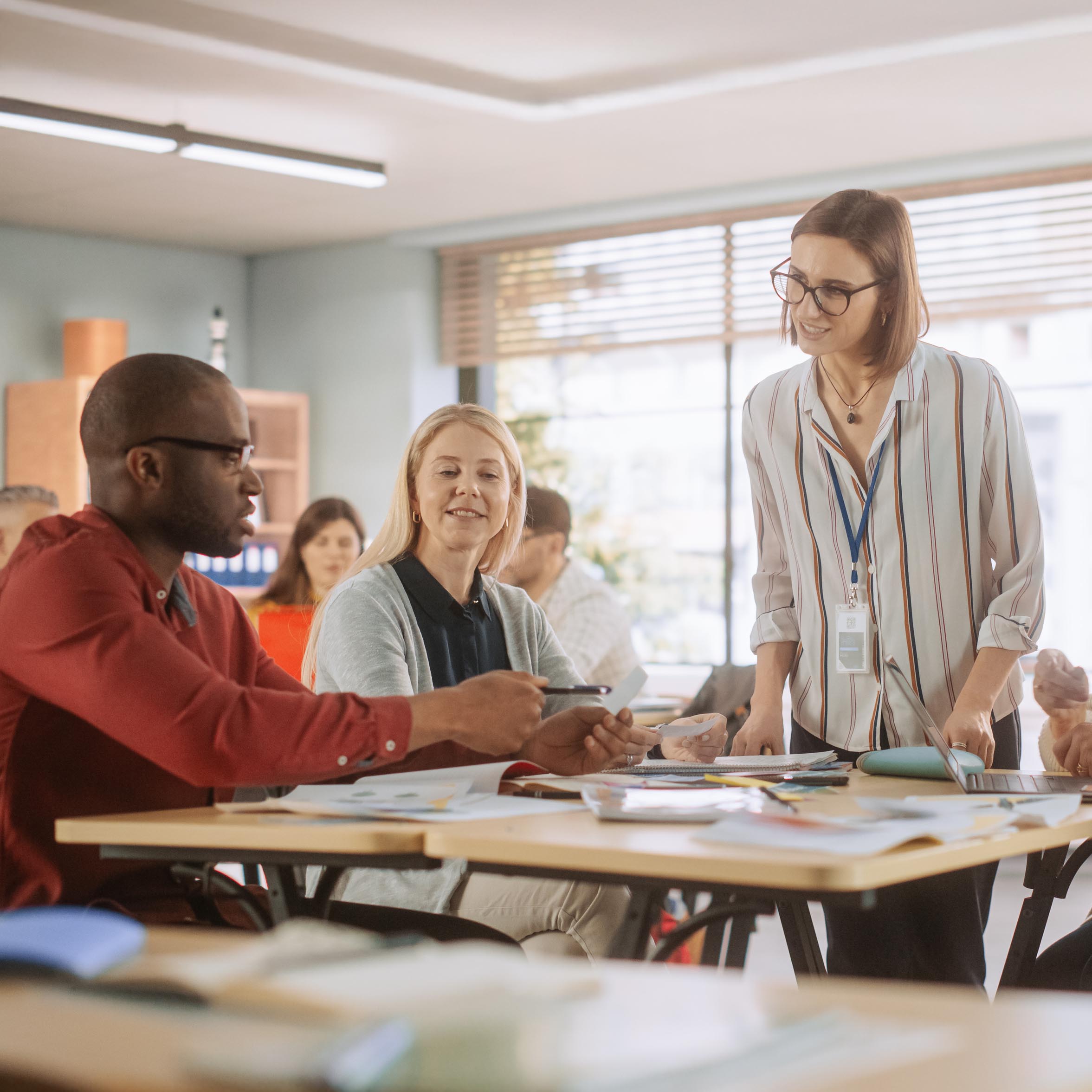 Adult Education Center: Adult Students Learning in Classroom, Working as Two Teams on a Verbal Education Game. Positive Female Teacher Giving Advice, Answering Questions, and Motivating Students